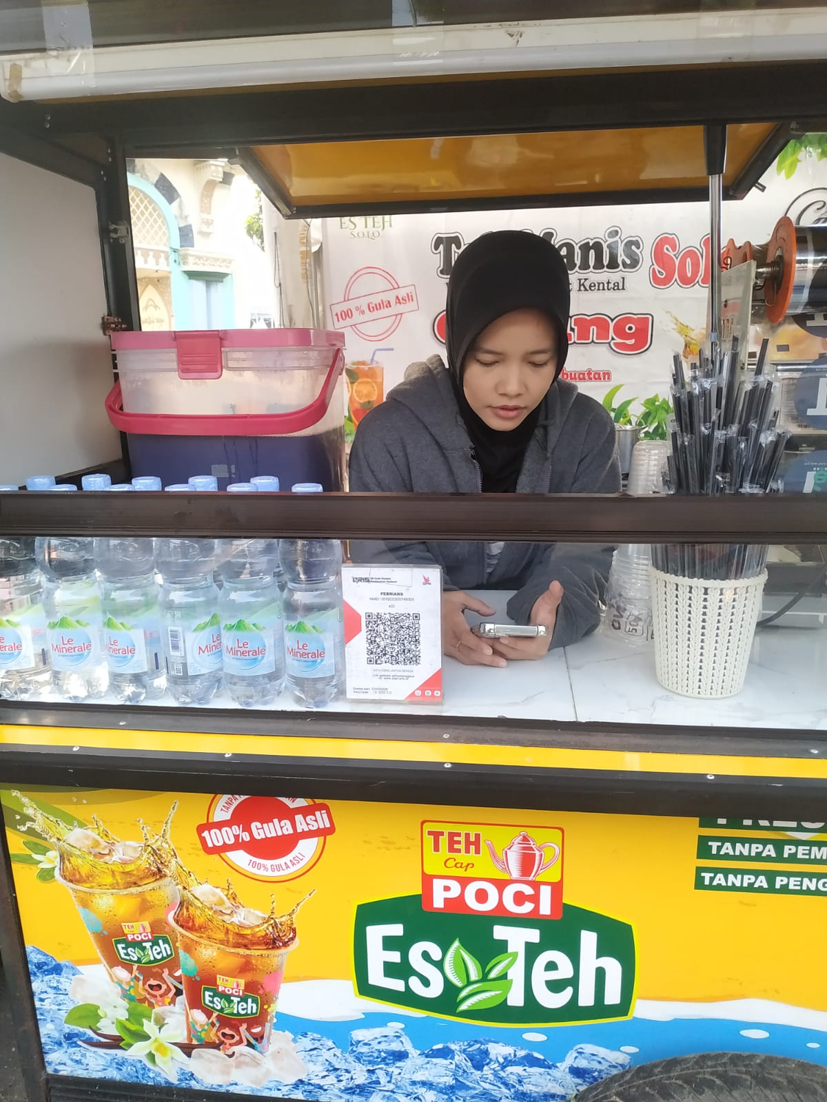 Della pedagang Es Teh Poci berhijab di gerobak kuning dengan QRIS di Taman Elektrik Masjid Raya Al-Azhom Tangerang