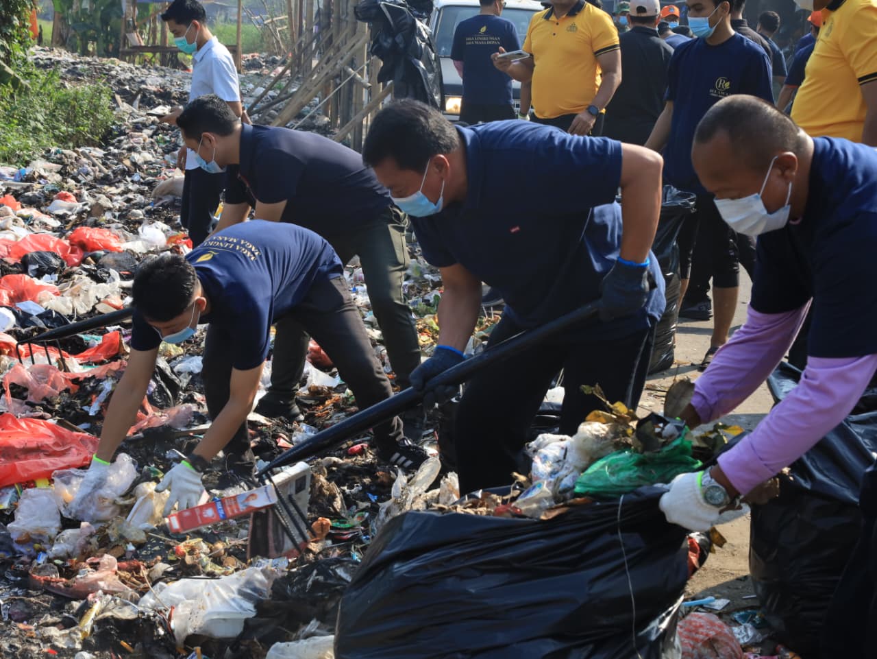 Bupati Tangerang Moch Maesyal Rasyid memakai kaos biru, topi dan masker memegang garpu sampah membersihkan tumpukan sampah bersama anggota TNI berseragam loreng saat kegiatan Jumat Bersih di Desa Tobat Balaraja 19 Juni 2026