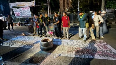 Orator mahasiswa berorasi di depan spanduk Cabut UU TNI-Polri sambil membakar ban saat demo tolak MBG di Tangerang