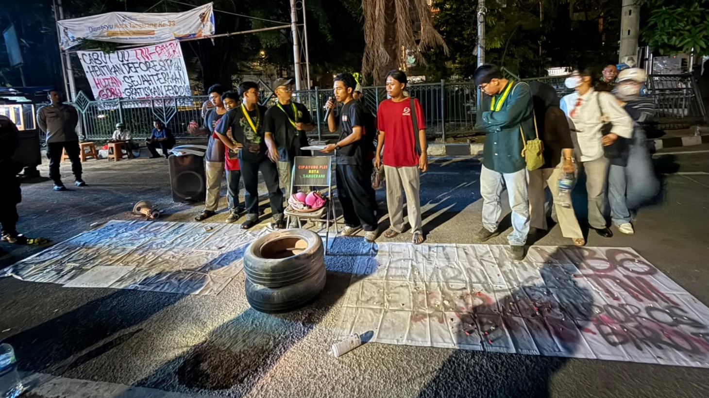 Orator mahasiswa berorasi di depan spanduk Cabut UU TNI-Polri sambil membakar ban saat demo tolak MBG di Tangerang