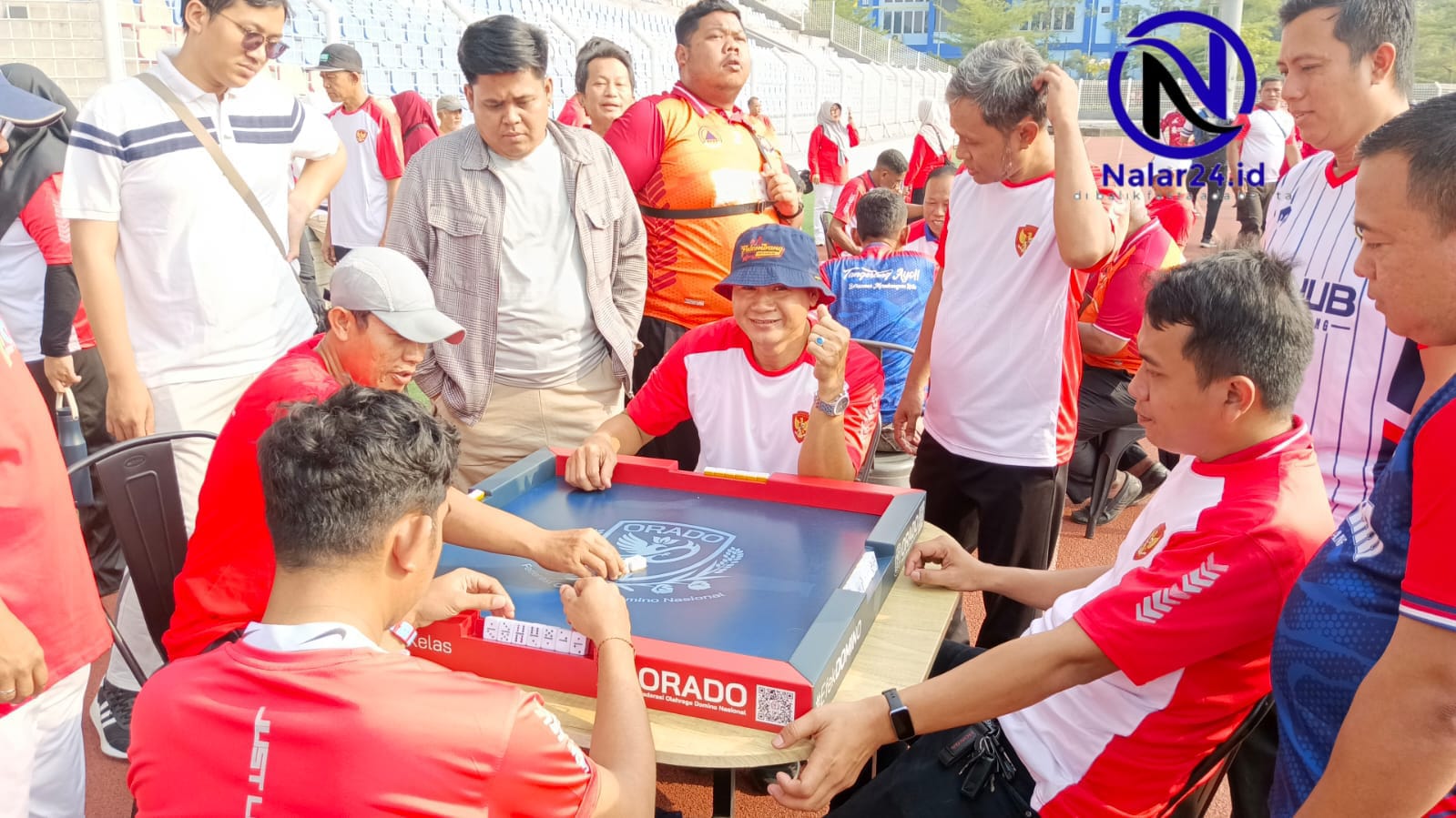 Pejabat memakai baju merah putih duduk main domino dikelilingi penonton