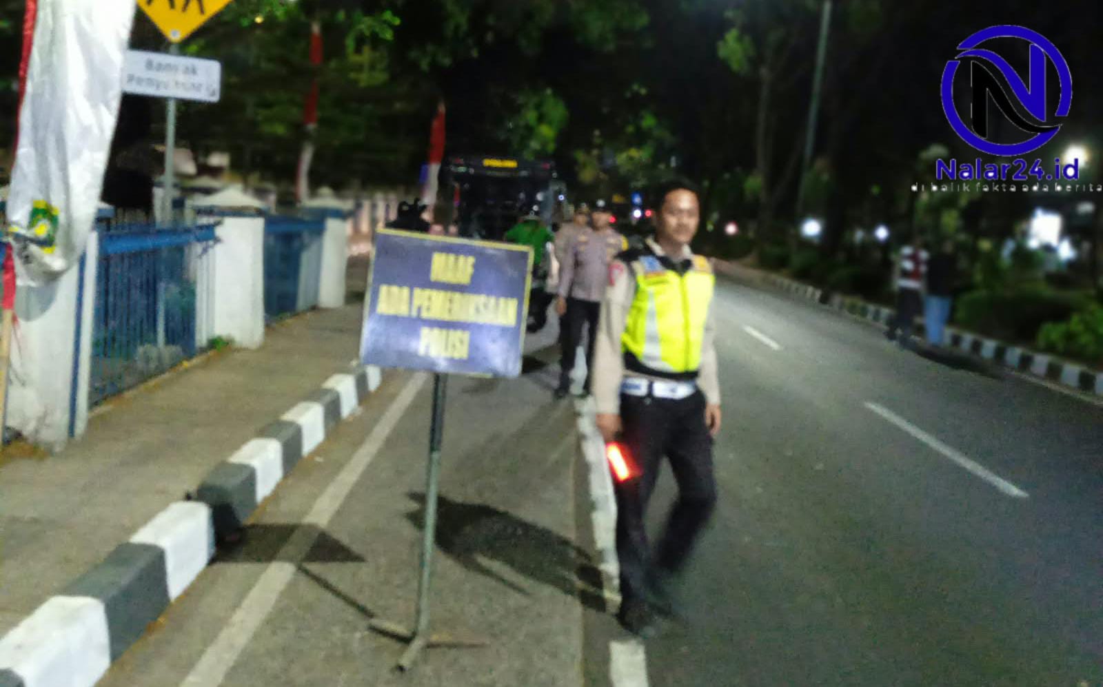 Seorang personel Satlantas Polsek Tangerang tampak berjaga sambil memegang lampu sorot.