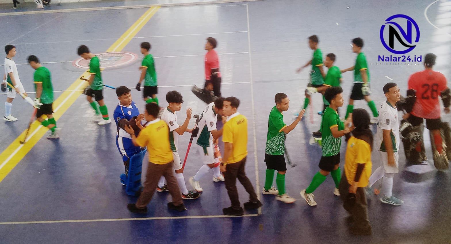 Para pemain hoki mengenakan jersey hijau dan putih saling bersalaman di tengah lapangan indoor setelah pertandingan selesai