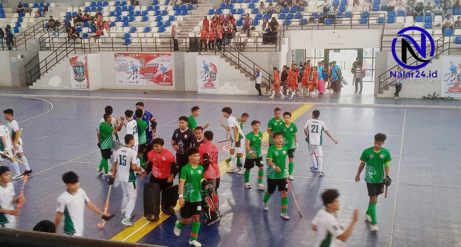 Sejumlah pemain hoki dengan jersey warna berbeda berjalan di atas lapangan indoor sambil membawa stick