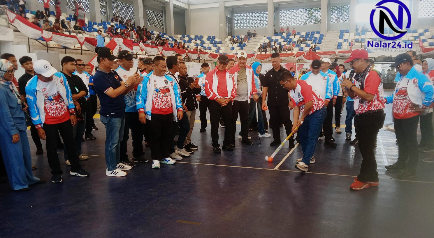 Seorang pejabat memegang stick hoki bersiap memukul bola di tengah lapangan disaksikan para tamu undangan