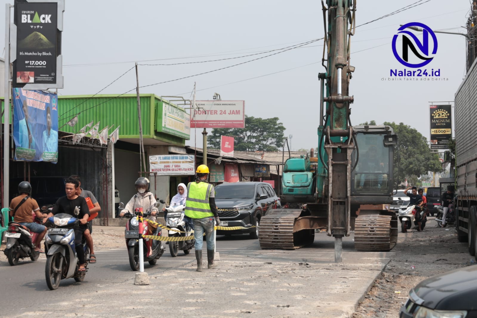 Sebuah alat berat ekskavator berwarna hijau sedang bekerja membongkar jalan di tengah kemacetan kendaraan motor dan mobil