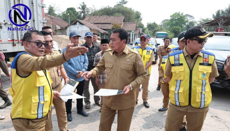 Seorang pejabat memakai seragam coklat sedang menunjuk dan berbicara dengan petugas yang mengenakan rompi kuning di pinggir jalan