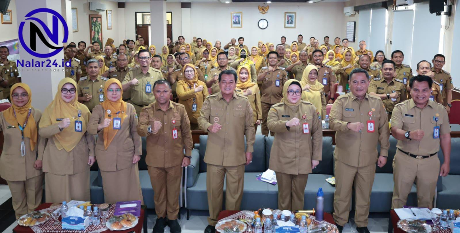 Sekelompok besar pegawai memakai seragam coklat berbaris dan mengepalkan tangan untuk foto bersama di dalam ruangan