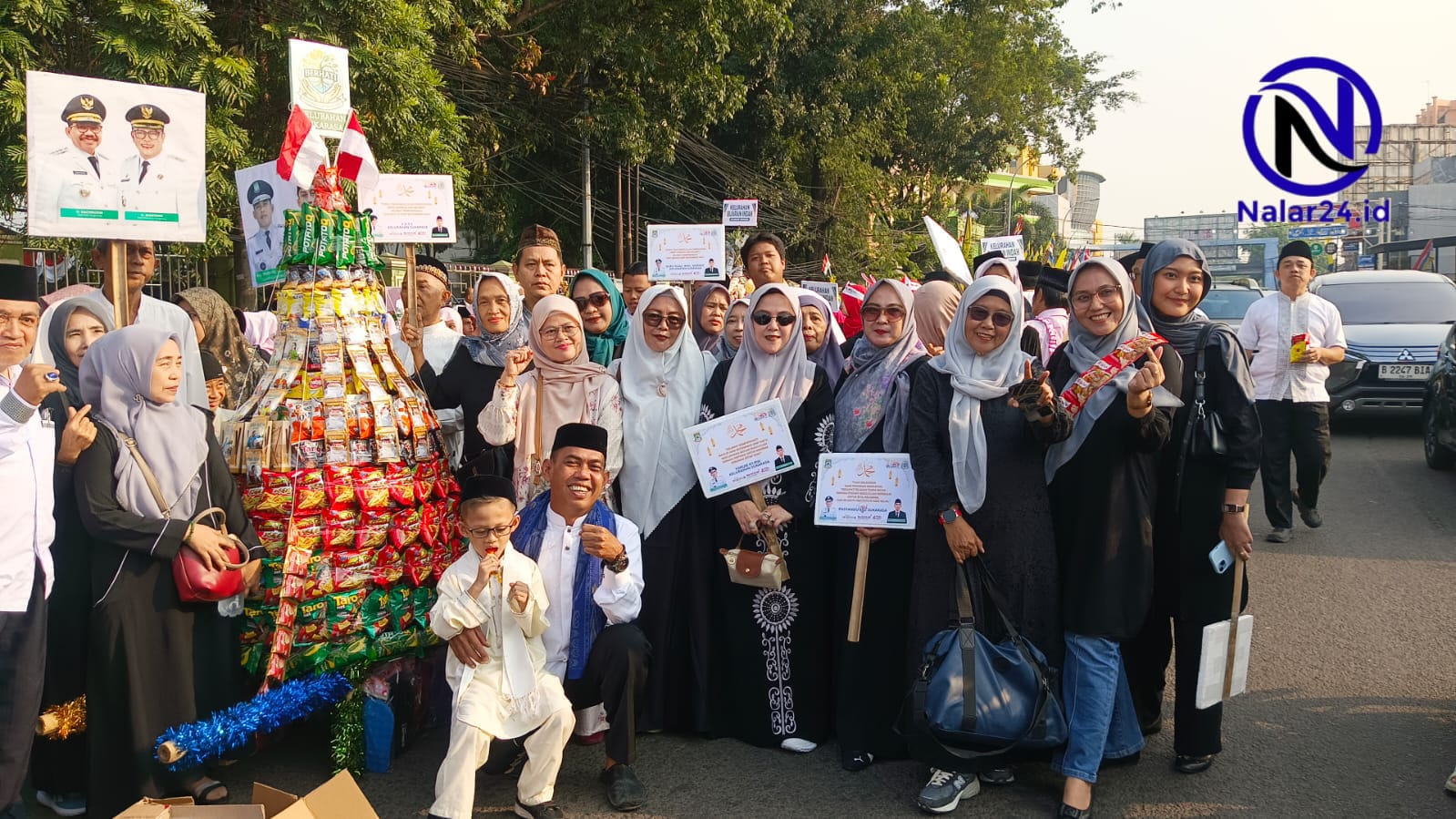 Sejumlah perempuan berhijab dan pria berpeci berpose di jalan bersama gunungan tinggi yang terbuat dari bungkusan makanan ringan