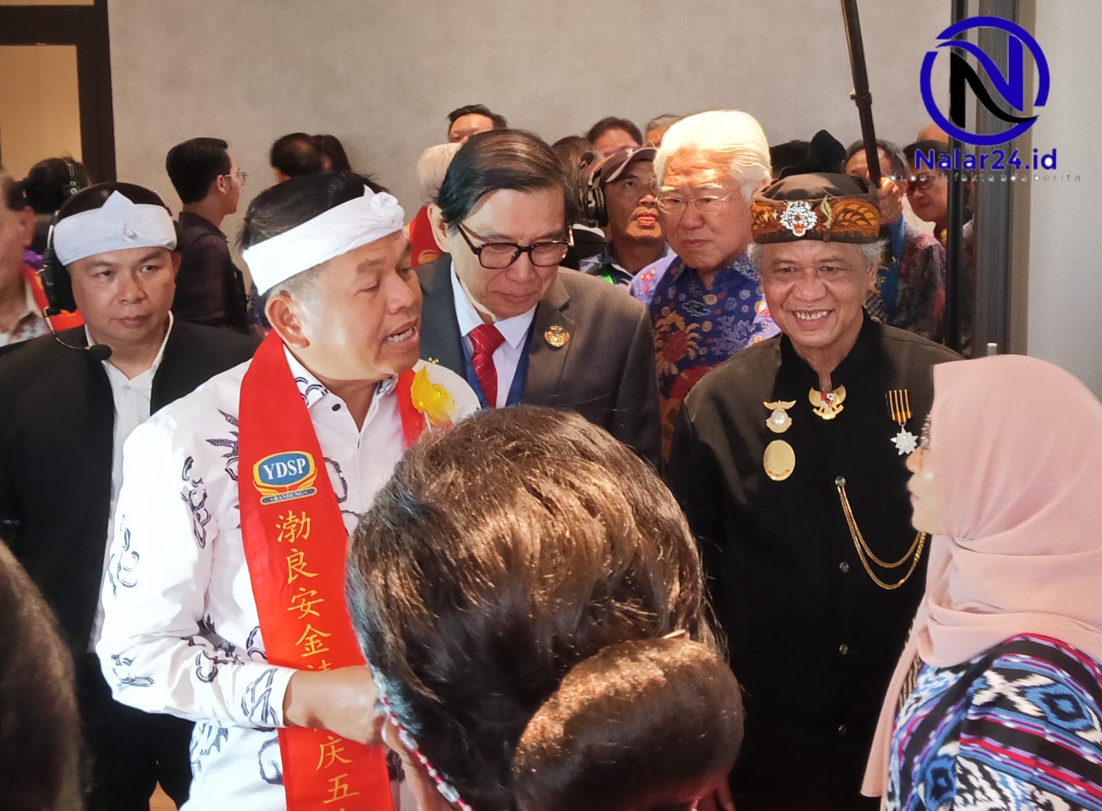 Dua orang pria, satu memakai ikat kepala putih dan satu memakai baju hitam adat Sunda dengan topi, sedang berbincang di kerumunan tamu