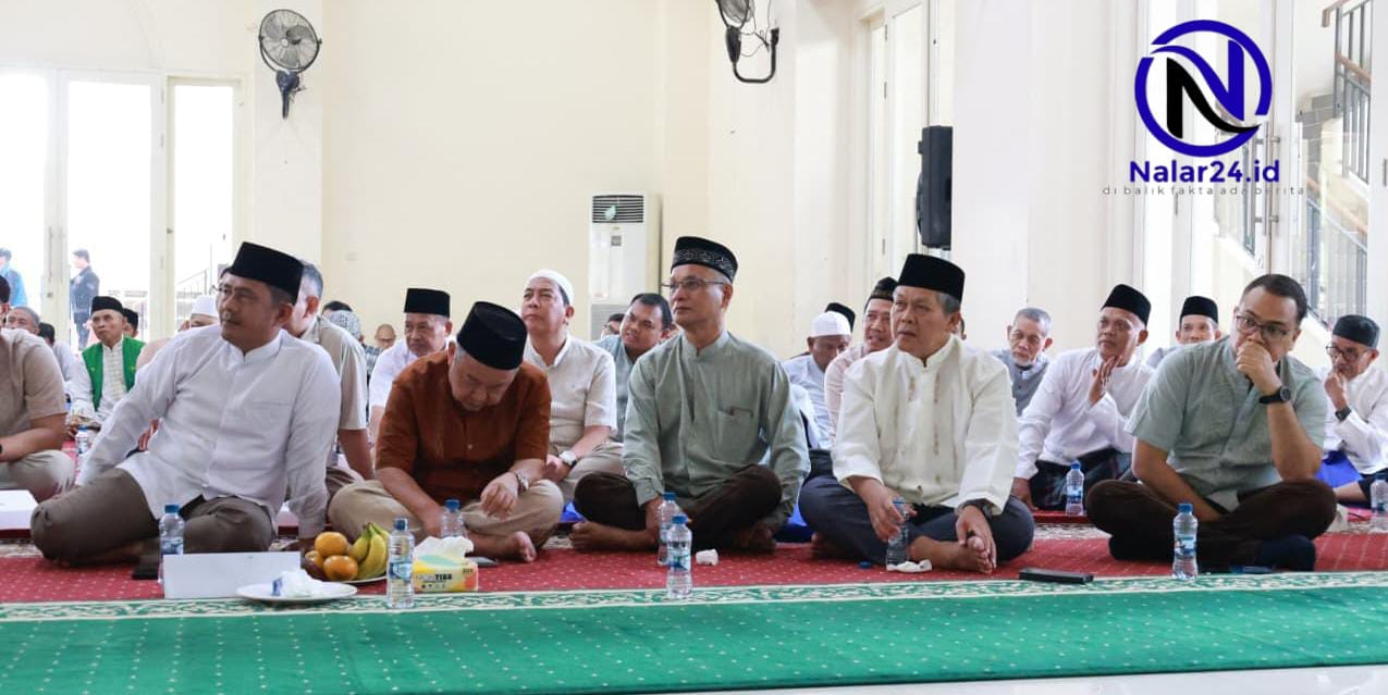 Beberapa pria memakai baju koko putih dan peci hitam duduk di lantai berkarpet merah hijau dengan air mineral dan buah di depan mereka