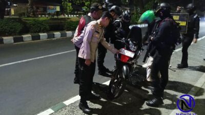 Sejumlah petugas polisi berbincang dengan dua orang pengendara motor di pinggir jalan saat malam hari