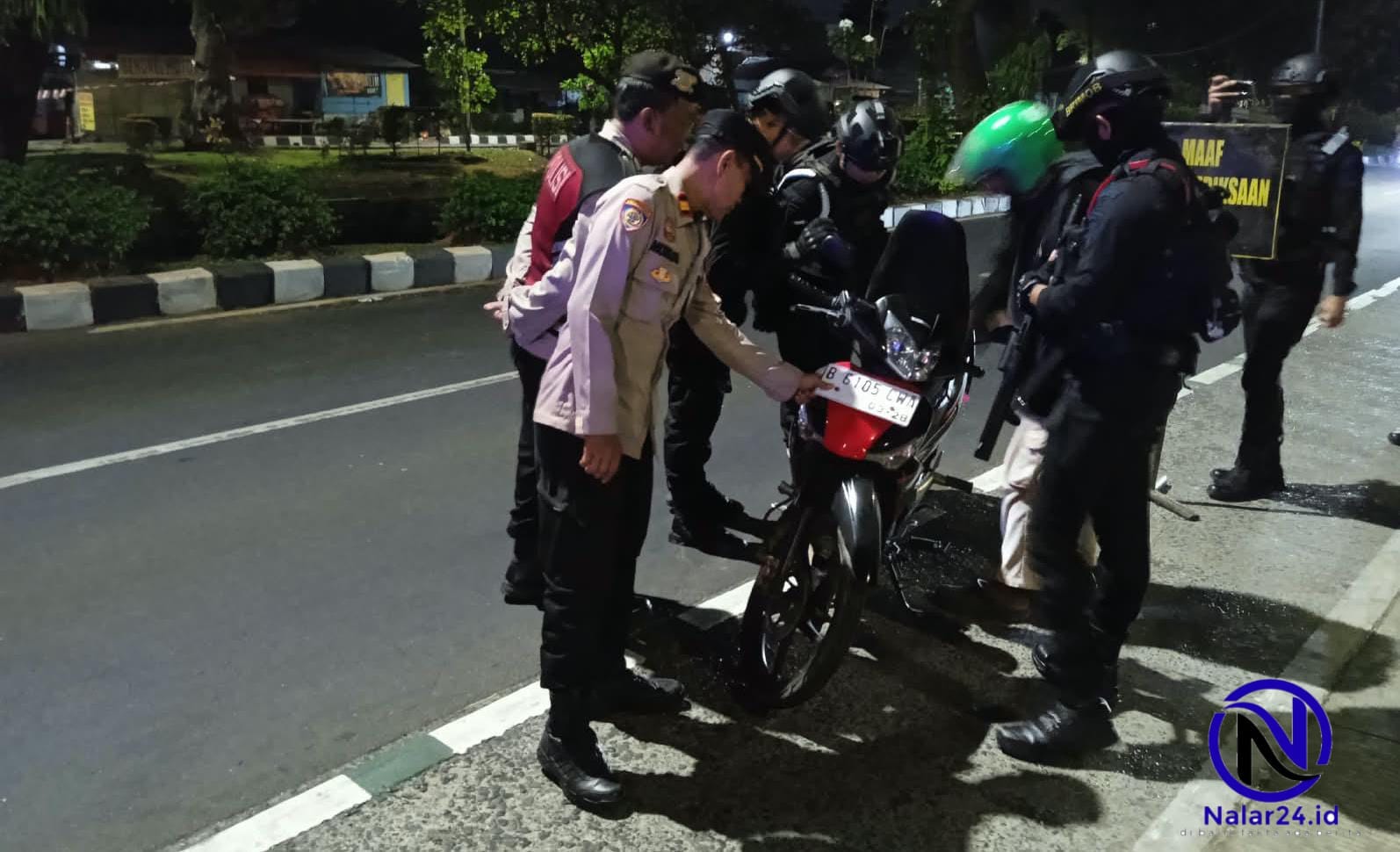 Sejumlah petugas polisi berbincang dengan dua orang pengendara motor di pinggir jalan saat malam hari