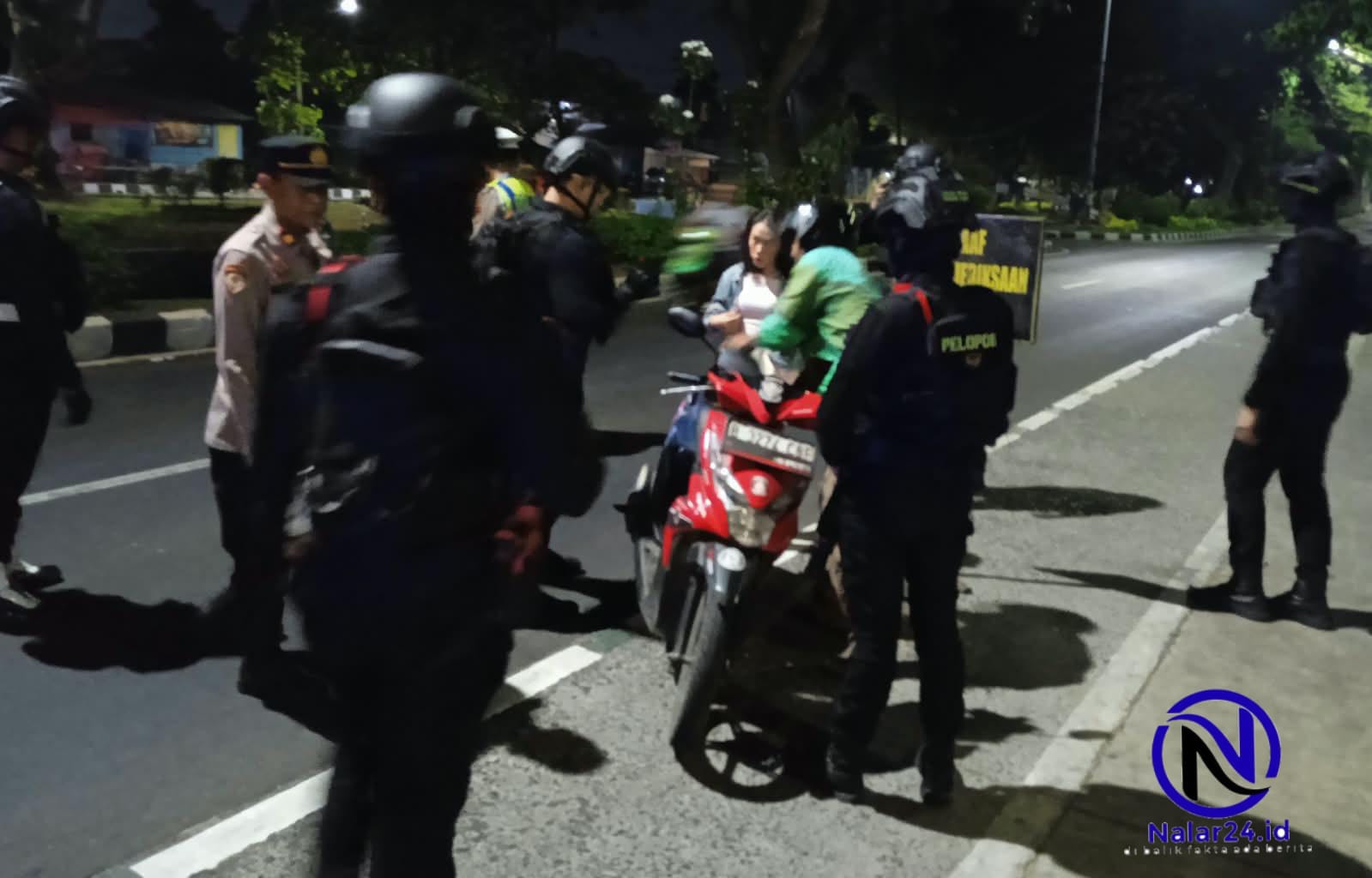 Seorang petugas polisi berbaju coklat menunjuk plat nomor motor yang sedang diperiksa oleh beberapa petugas lain